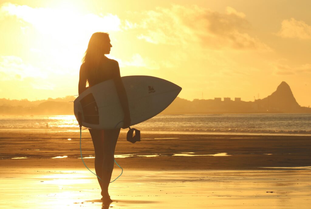 Mulher Segurando A Prancha De Surfe Em Pé Na Costa Durante O Pôr Do Sol · Foto profissional gratuita