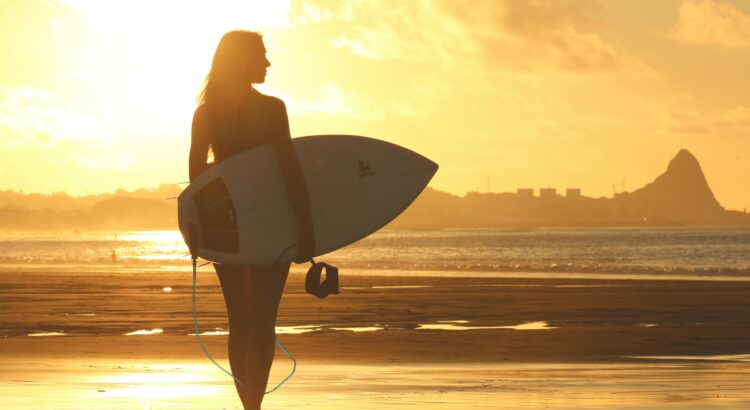 Mulher Segurando A Prancha De Surfe Em Pé Na Costa Durante O Pôr Do Sol · Foto profissional gratuita